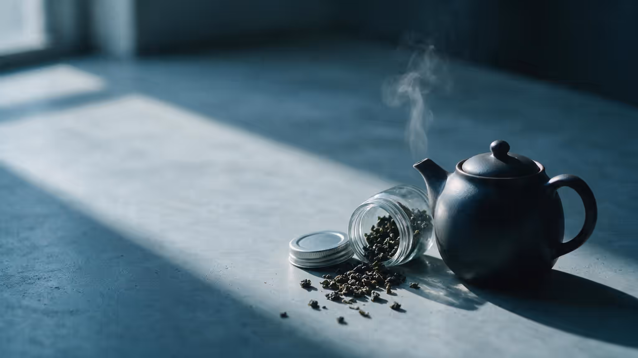 深色陶壺與傾倒的烏龍茶葉罐，冷調光線下的茶桌
